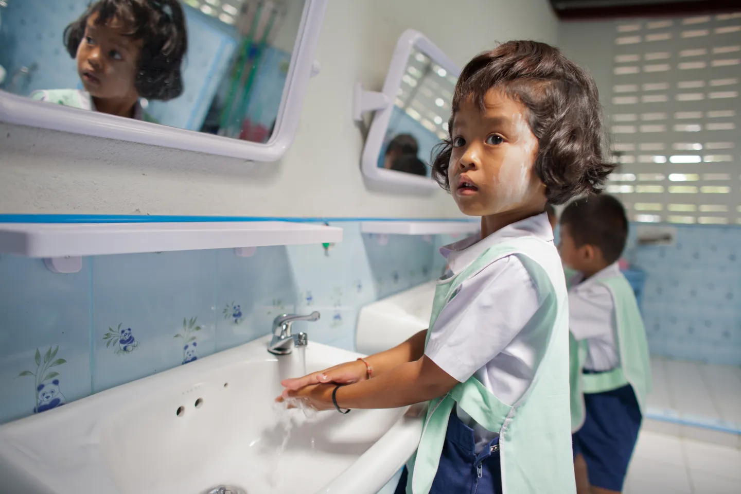 A little girl in a student uniform is washing her hands at the basin.