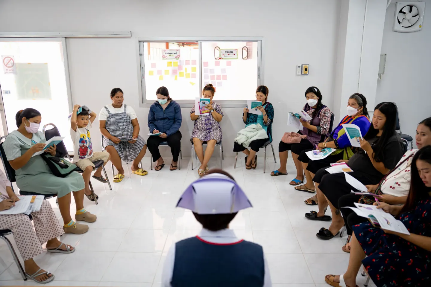 A group of women sitting in a circle in a bright room, reading informational booklets while a nurse sits facing them.