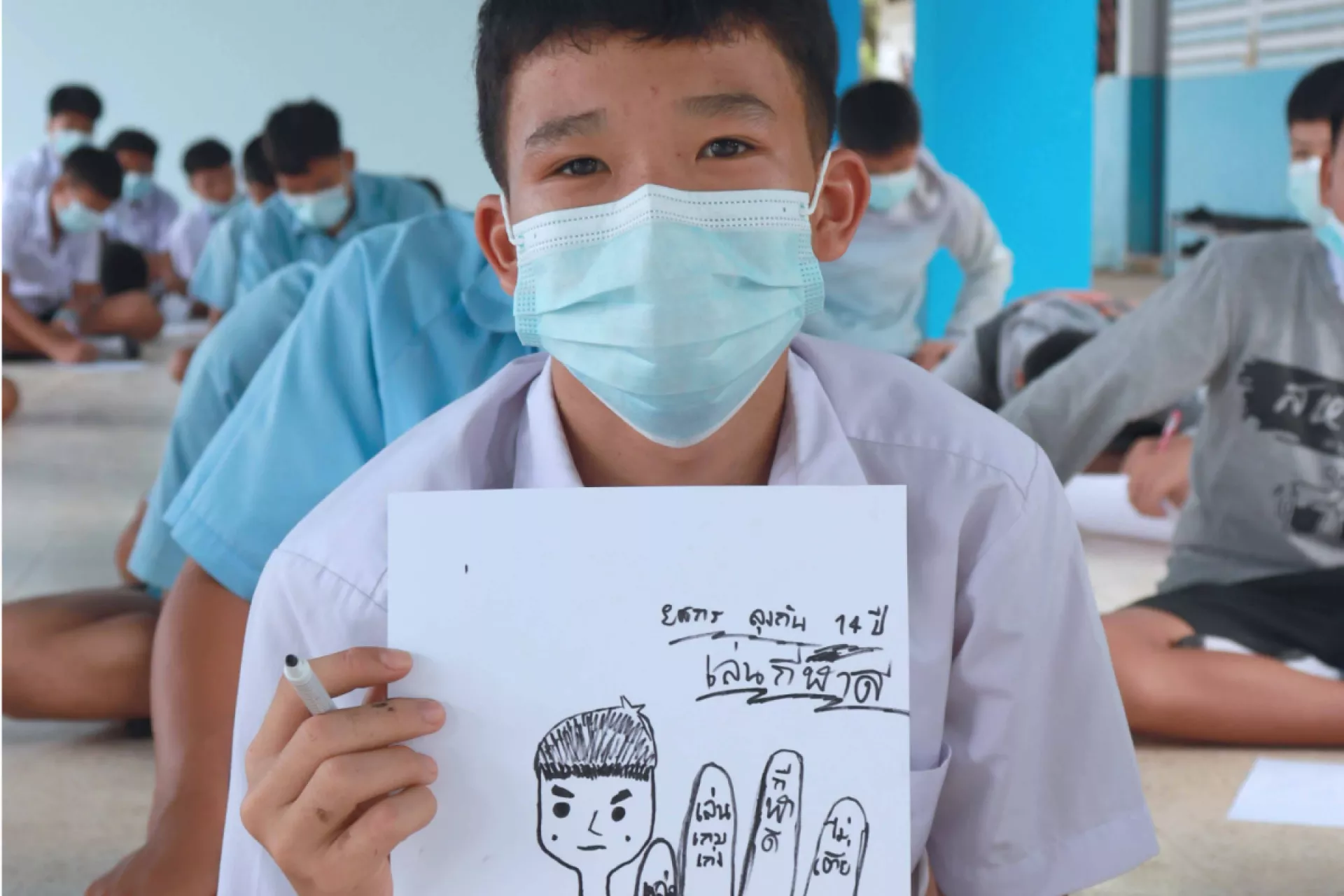 A student wearing a face mask is showing his drawing.
