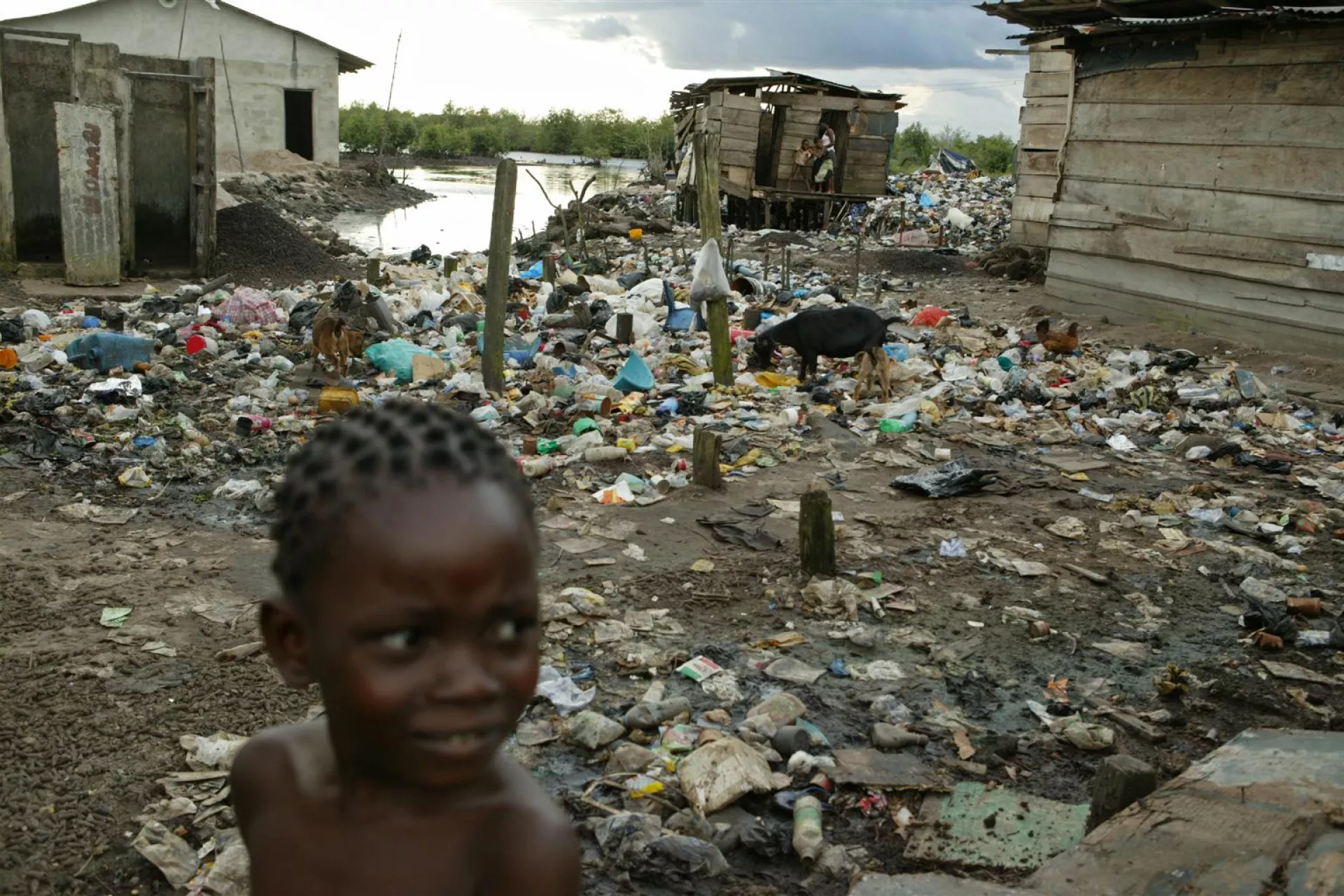 a girl stands amid garbage, mud and human waste in an impoverished waterside community