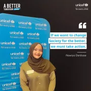 A young woman wearing an olive-green hijab and matching shirt is smiling while standing in front of a blue UNICEF backdrop with the text &amp;quot;UNICEF for every child&amp;quot; repeated across it. The right side of the image features a solid black background with a quote: &amp;quot;If we want to change society for the better, we must take action. - Nawiya Denbase.&amp;quot; Additional text reads &amp;quot;A Better Tomorrow Today&amp;quot; in the top left corner and &amp;quot;UNICEF for every child&amp;quot; in the top right corner.