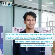 A young man with short black hair is smiling while wearing a dark blue shirt over a black undershirt. He is standing indoors in front of a glass wall and posters featuring children. The image includes a quote: &amp;quot;As a UNICEF volunteer, my role is to empower children with the knowledge of 'development.' We show them that their potential is a key driver of societal growth. - Goey Wisit Kongkam.&amp;quot; Additional text reads &amp;quot;A Better Tomorrow Today&amp;quot; in the top left corner and &amp;quot;UNICEF for every child&amp;quot; in the top right.