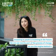 A young woman with long dark hair is smiling while leaning on a railing surrounded by greenery. She is wearing a black polo shirt with the logo &amp;quot;iMC&amp;quot; on it and sunglasses resting on her head. The background features a brick wall with hanging plants. The image includes a quote. Additional text reads &amp;quot;A Better Tomorrow Today&amp;quot; in the top left corner and &amp;quot;UNICEF for every child&amp;quot; in the top right corner.