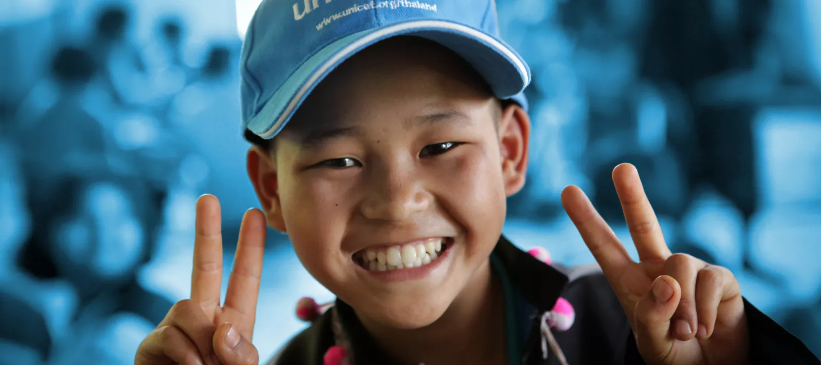 A boy wearing UNICEF cap is smiling.