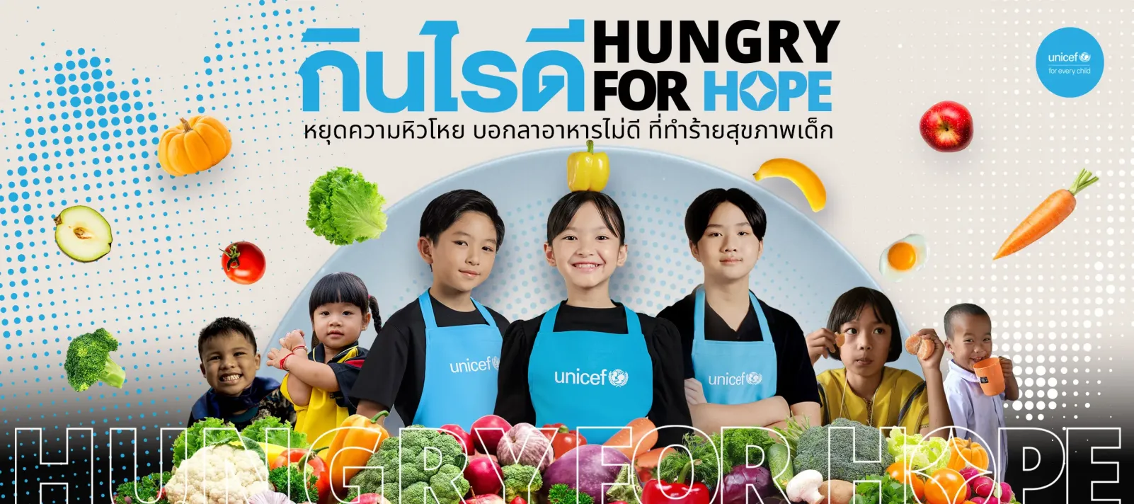 เด็กสวมผ้ากันเปื้อนยูนิเซฟยืนยิ้มท่ามกลางผักและผลไม้หลากสี ภาพมีข้อความว่า &ldquo;กินไรดี Hungry for Hope &ndash; หยุดความหิวโหย บอกลาอาหารไม่ดี ที่ทำร้ายสุขภาพเด็ก&rdquo;