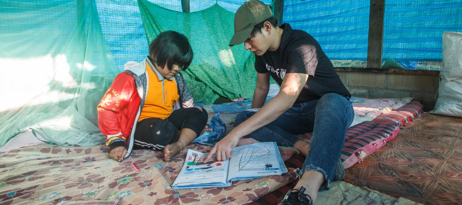 Peck Palitchoke is talking to a little girl while pointing at the content in the book.