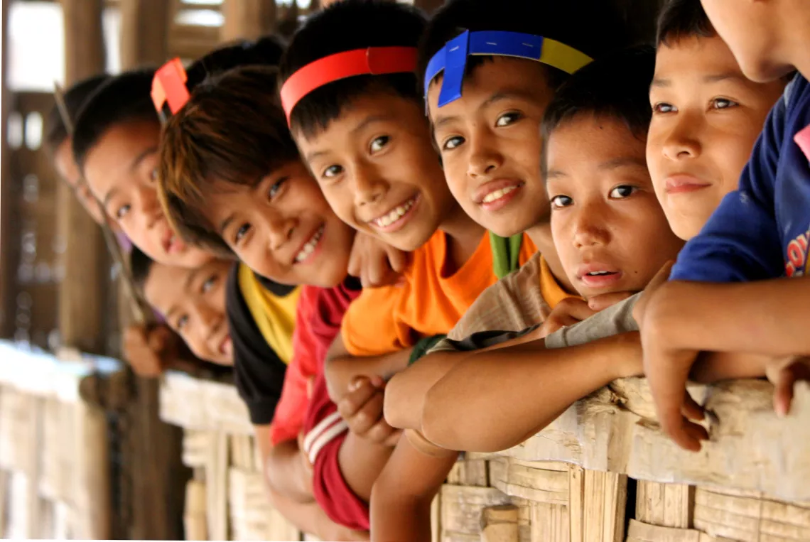 A group of boys and girls leaning out from the window, smiling and looking at the camera.