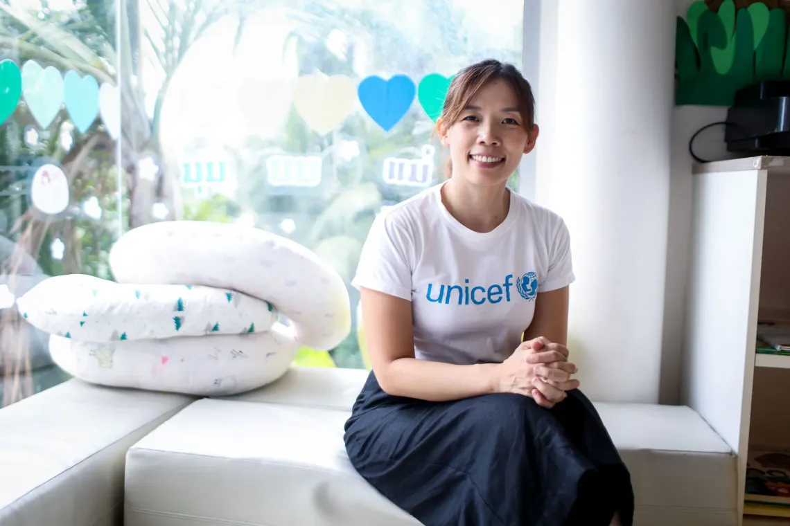 A woman sitting in a bright room nearby the window.