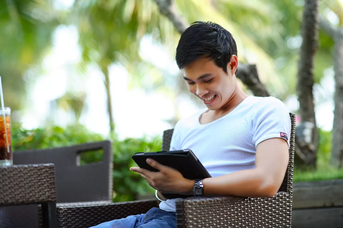 A young man wearing light-colored t-shirt is checking something using a tablet.
