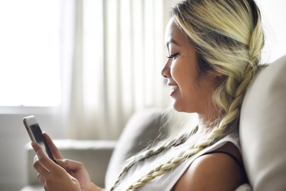 A young blond girl using her smartphone, smiling.