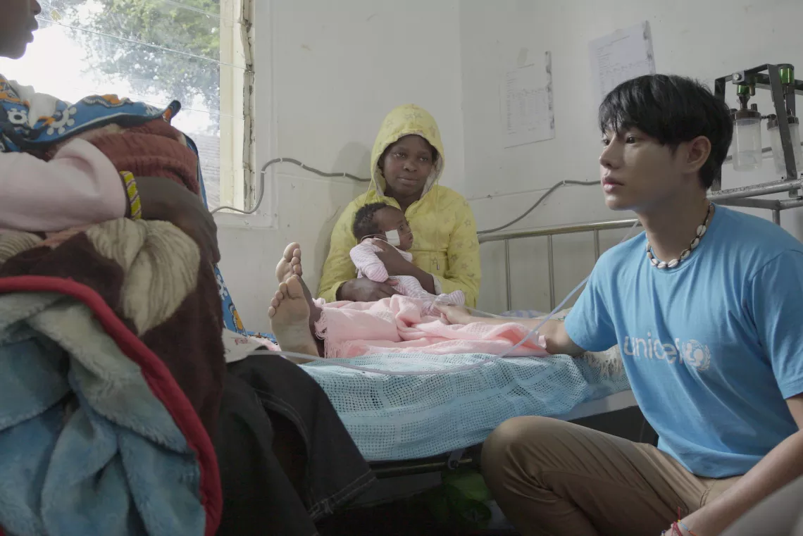 Peck Palitchoke is sitting beside the bed talking to a mother holding her sick little child.