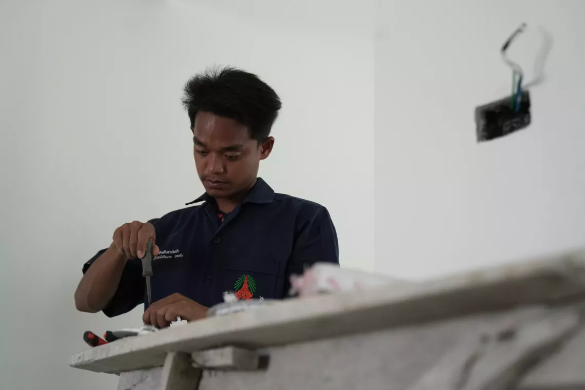 A man in a dark uniform concentrates while working with a screwdriver on an electrical component at a construction site.