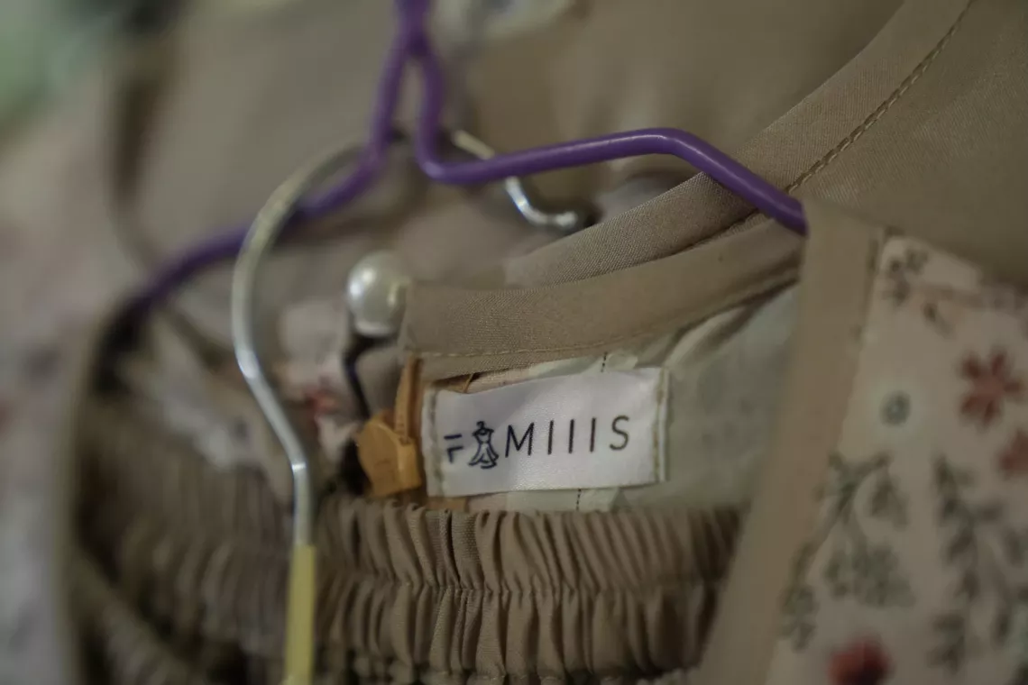 Close-up of a beige garment with a floral pattern on a hanger, showing a clothing label that reads "Famiiis" with a small dress icon.