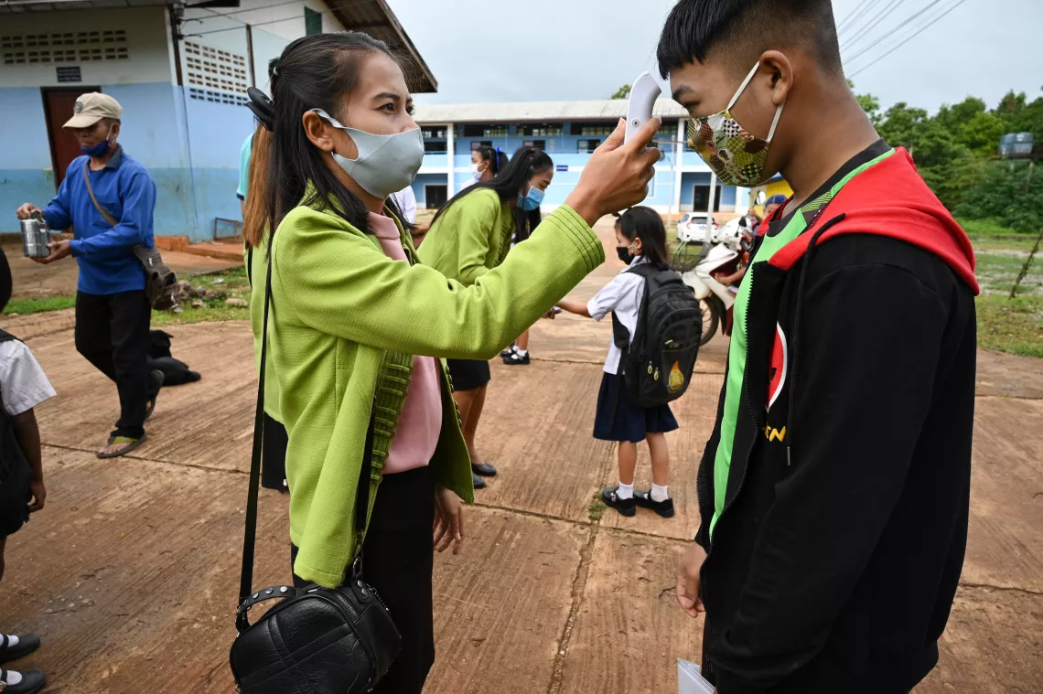 A female teacher is measuring a male student's body temperature at the screening area inside the school.