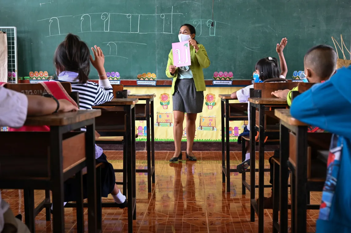 A female teacher is teaching her students how to read Thai alphabet at the front of the classroom.