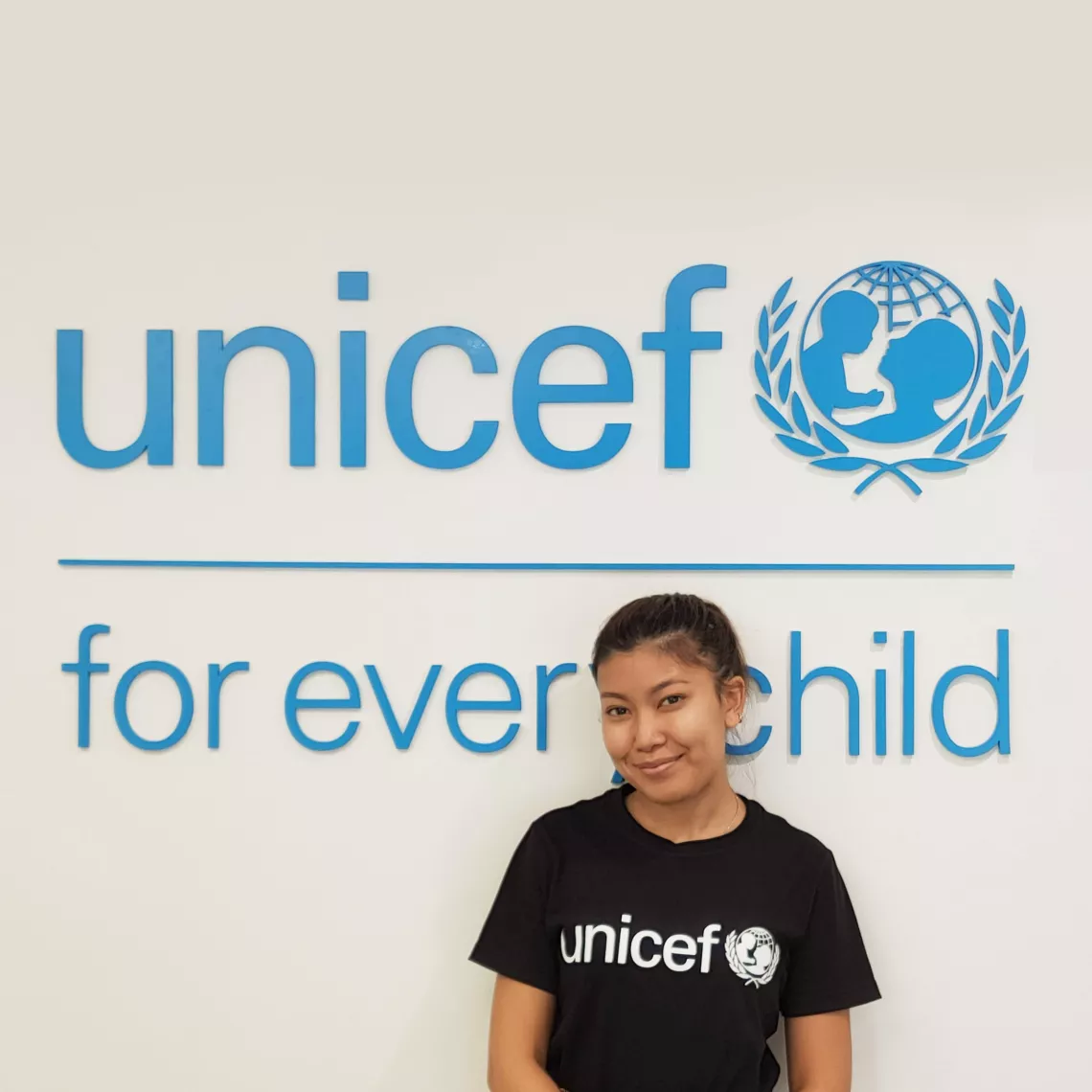 A lady in black UNICEF T-shirt standing in front of UNICEF big cyan logo.