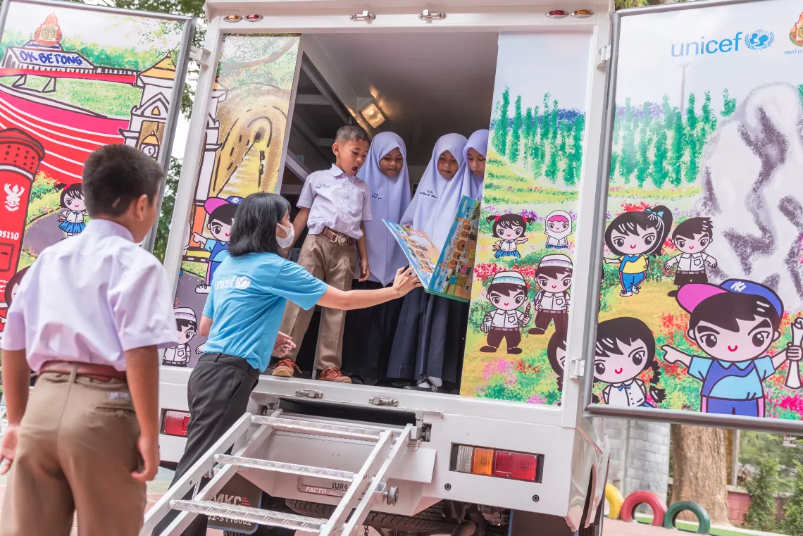 UNICEF staff encourages young students to pick up their favourite books from the Mobile Library.