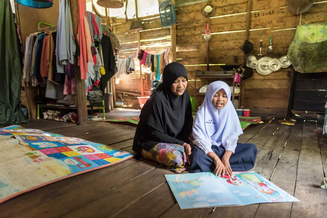 A Muslim child and her mother are sitting and reading book in their house.