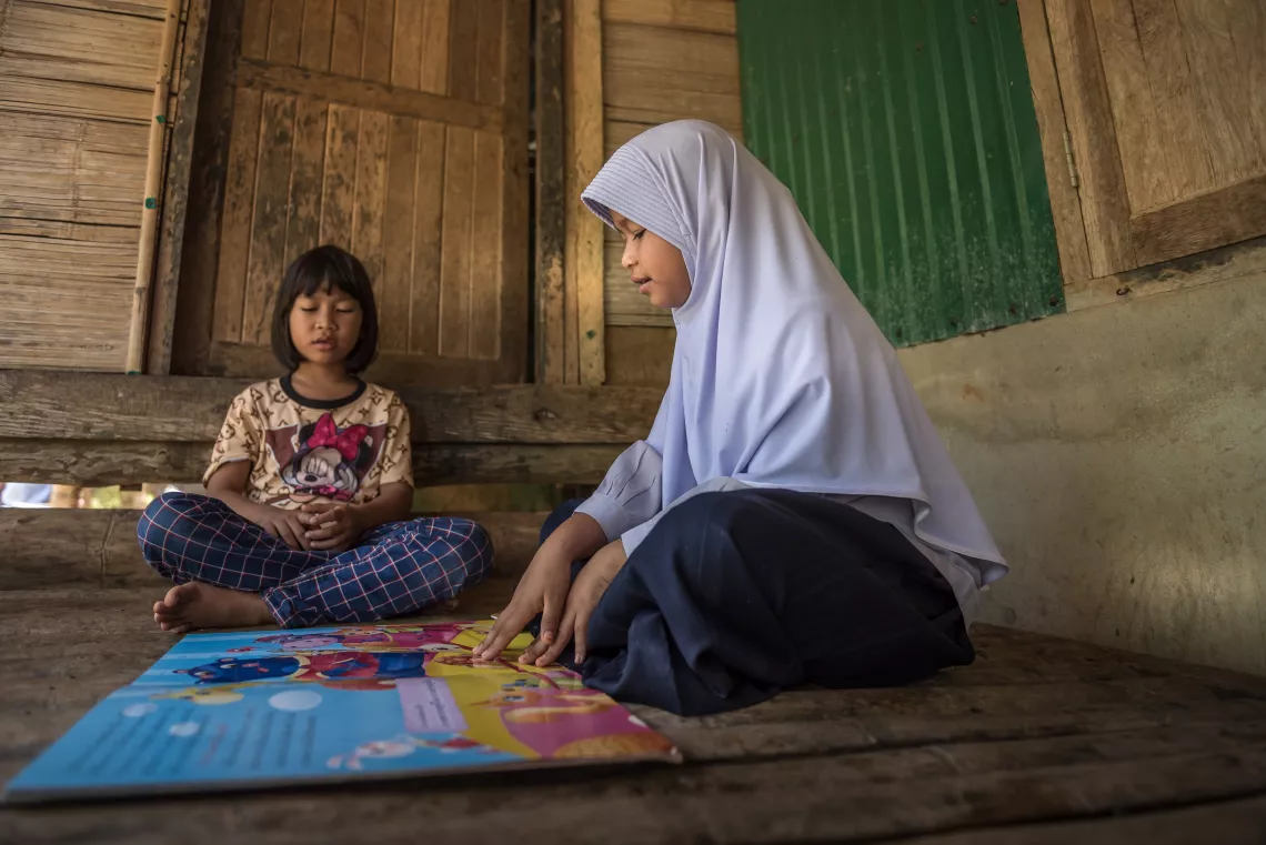 A school student and her younger sister are reading book together.