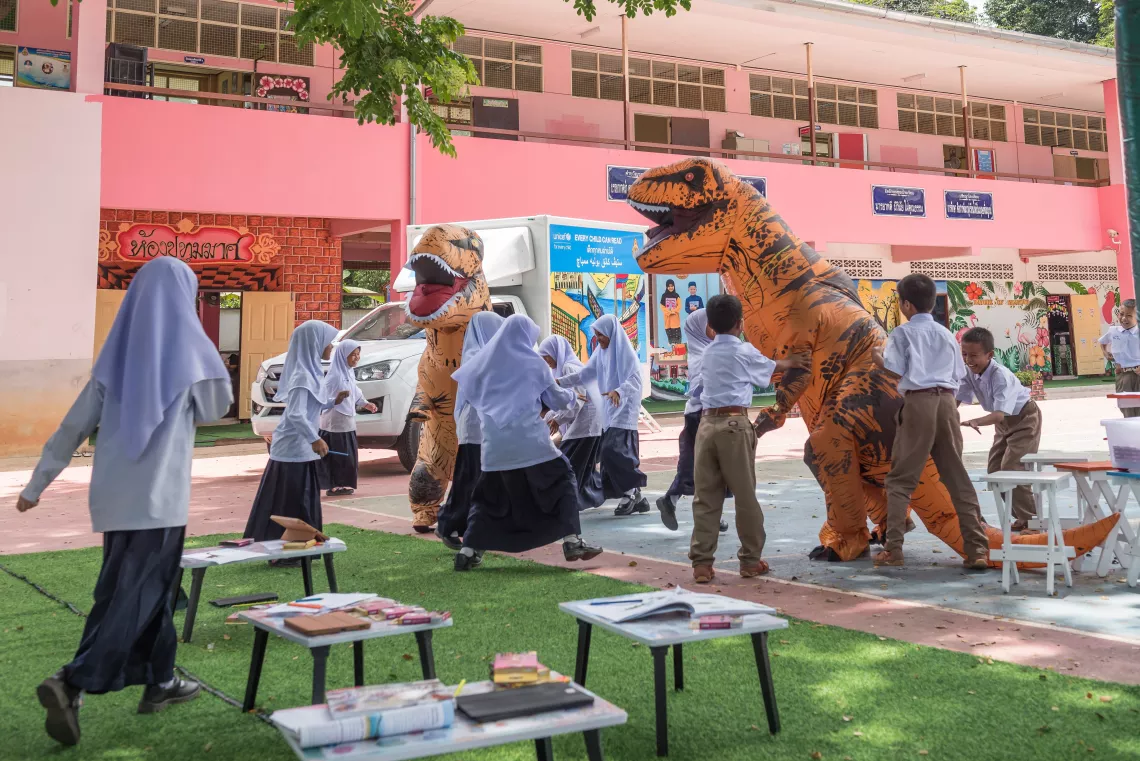 School children are playing around with dinosaur mascots.