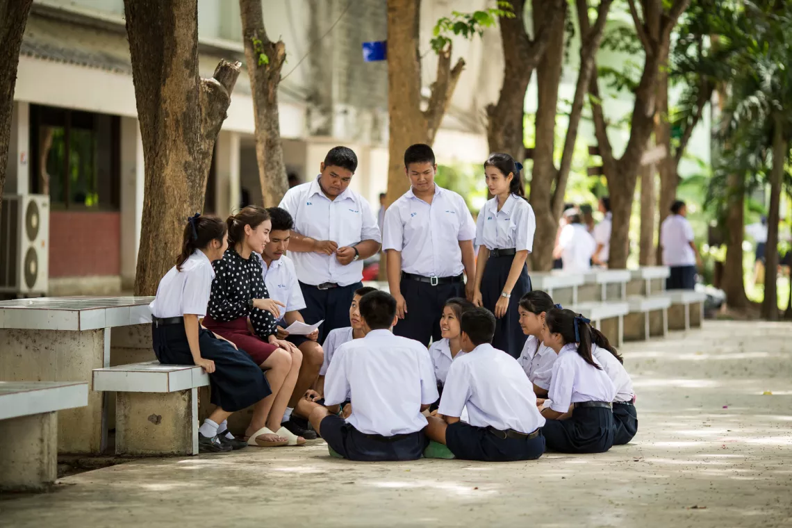 กลุ่มนักเรียนชายและหญิงกำลังห้อมล้อมคุณครู เพื่อพูดคุยกัน ในสวนของโรงเรียน