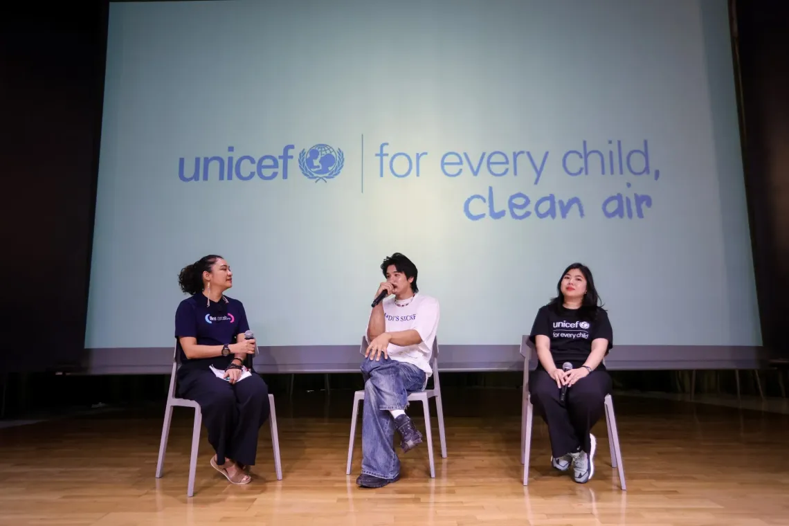 Three speakers sit on stage holding microphones during a discussion, with a screen behind them displaying the UNICEF message &ldquo;for every child, clean air.&rdquo;