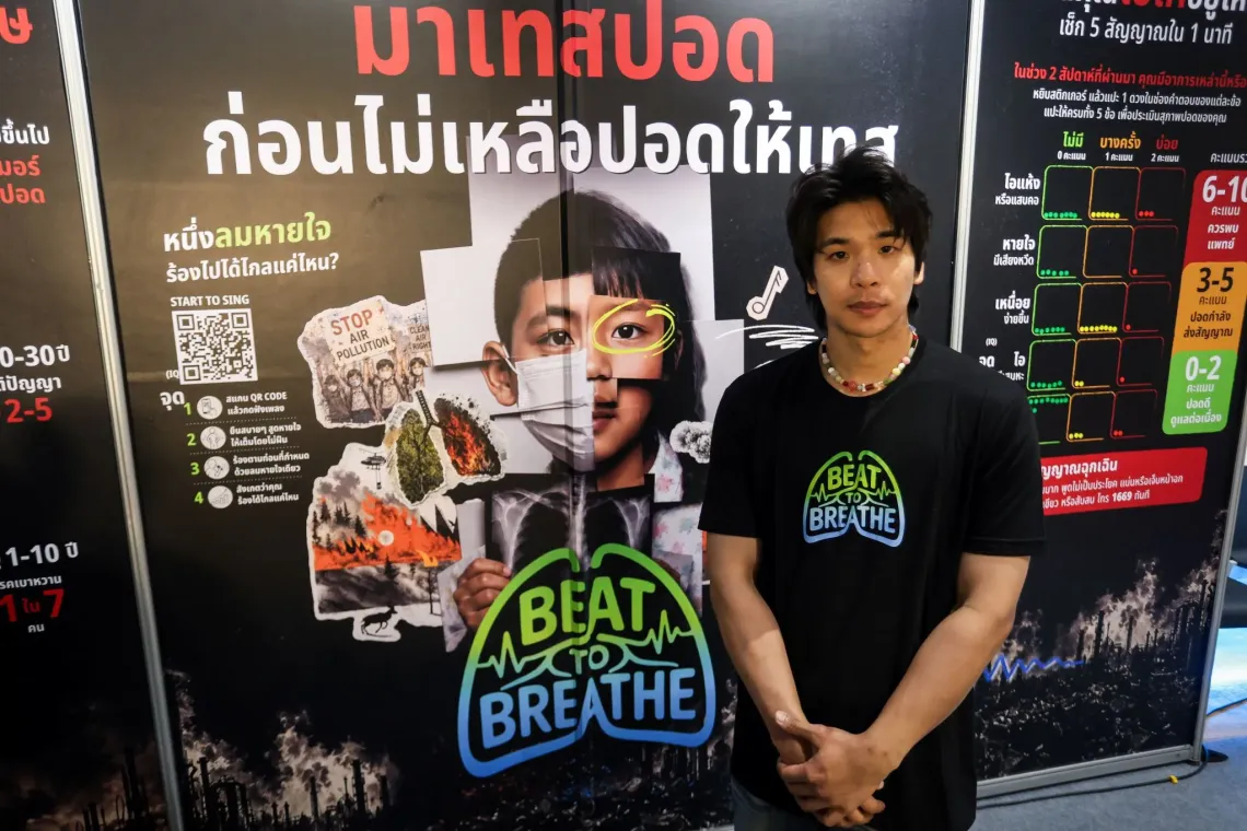 TangBadVoice wearing a &ldquo;Beat to Breathe&rdquo; campaign T-shirt stands beside a campaign display about air pollution and its effects on breathing.