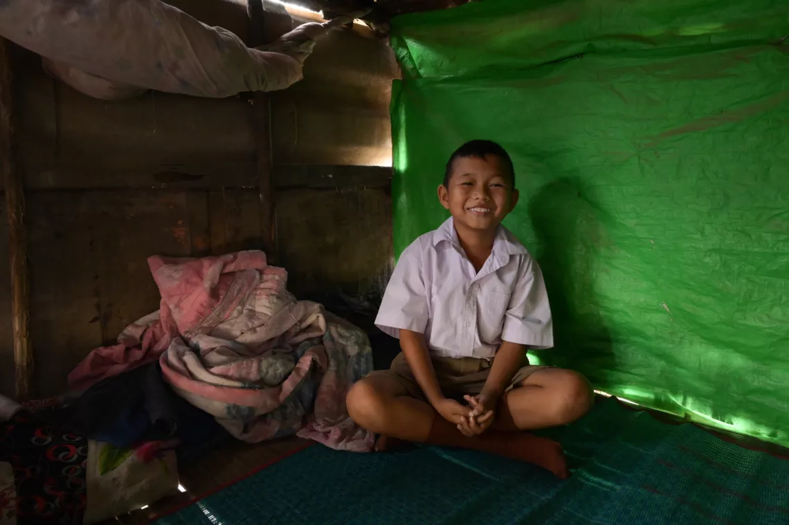 A young male student is sitting cross-legged, smiling.