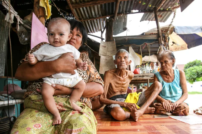 A family of grandparents, a mother and a baby. The mother is holding a baby, facing the camera.