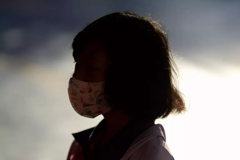 A silhouette of a young girl wearing a patterned face mask.