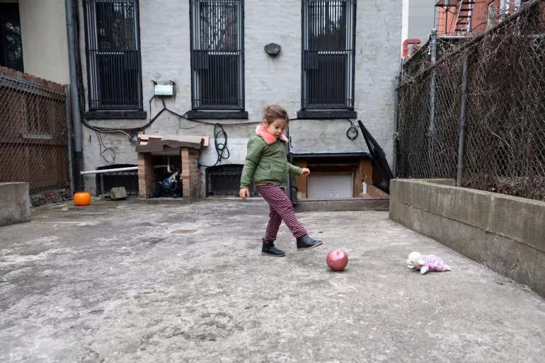 Young child plays with a ball in the backyard of an apartment building.