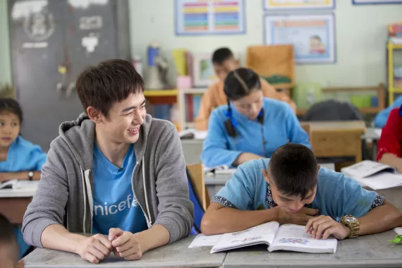 ินิชคุณ หรเวชกุล กำลังนั่งยิ้มมองเด็กนักเรียนชายที่กำลังนั่งอ่านหนังสืออยู่ข้างๆ
