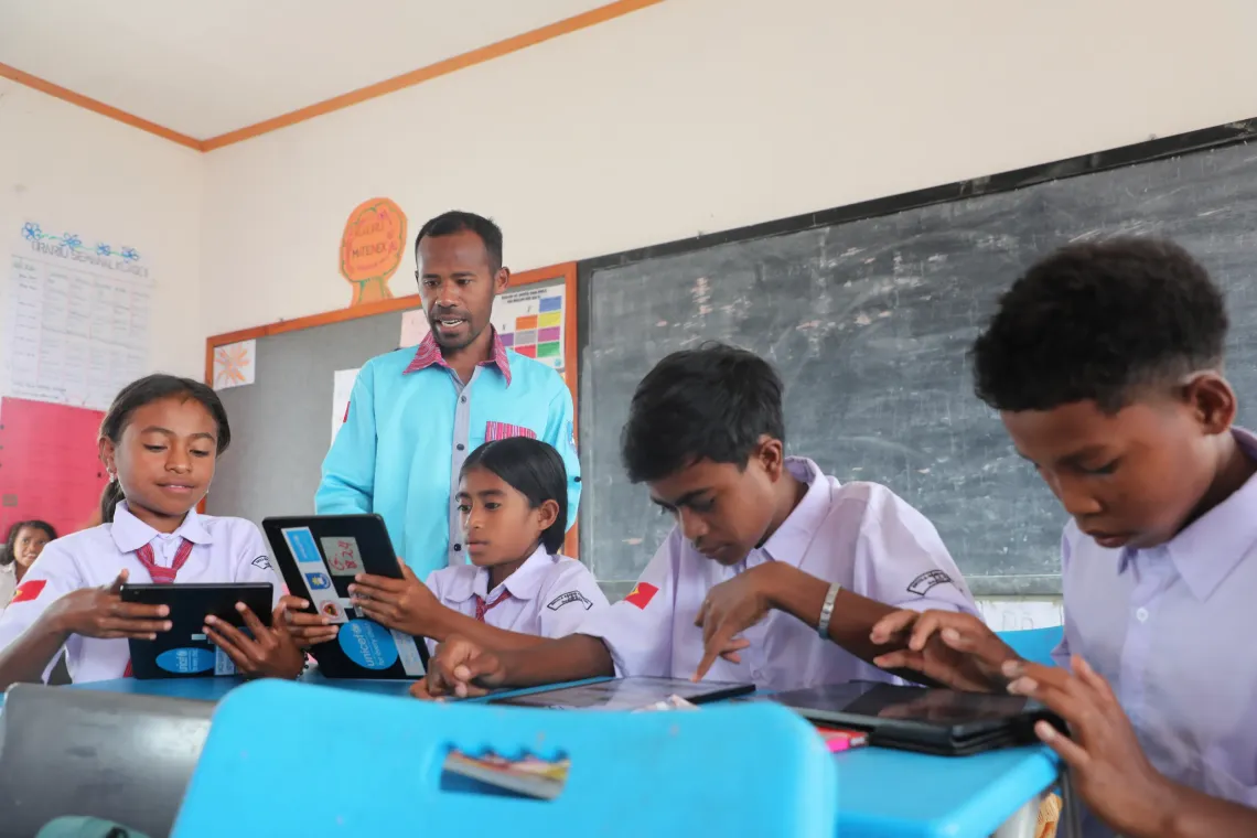 Teacher Marcelino guides Etelvina, Ericson, and their classmates as they use tablets to access the Eskola ba Uma/EbU (Learning Passport) platform. 