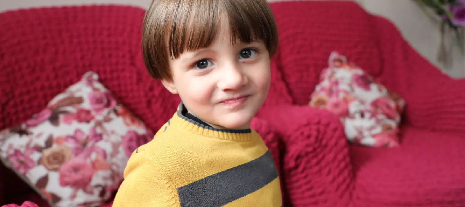 A little child smiles to the camera inside the living room of his house. 