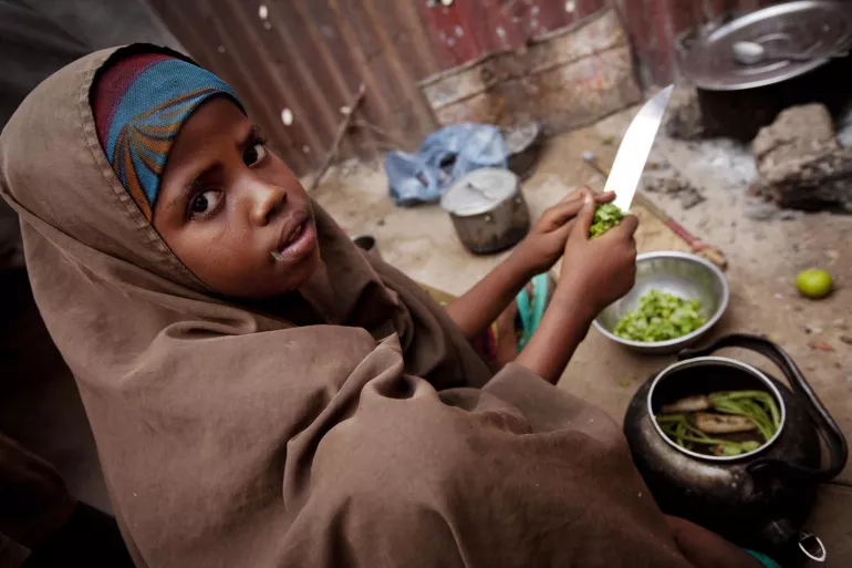 A girl helps prepare her family&rsquo;s evening meal, outside their makeshift home, in the Majo camp for displaced people, in Mogadishu, the capital.