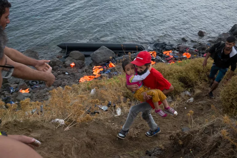 On 28 September, an Afghan volunteer from the NGO ActionAid carries Zarah Nabizadeh, 5, a newly arrived refugee from Afghanistan, along the shores near the town of Mithymna, on the island of Lesbos, in the North Aegean region. Zarah just arrived with her mother. The shore is lined with life jackets left behind by refugees.
