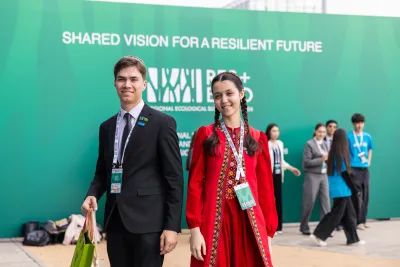 Two young participants wearing event badges smile in front of a green backdrop reading &ldquo;Shared vision for a resilient future&rdquo; at the Regional Ecological Summit 2026.
