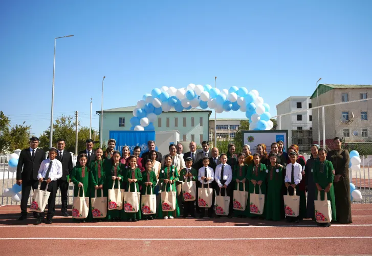 Schoolchildren in traditional green and black dress standing on the school steps beside teachers and UNICEF officials during an opening ceremony.