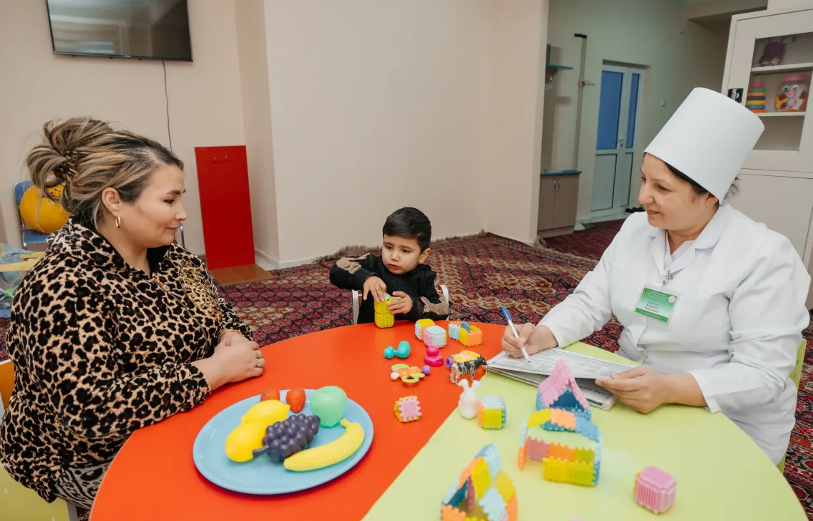 A healthcare professional consults with a mother and her young child during a developmental assessment using educational toys.