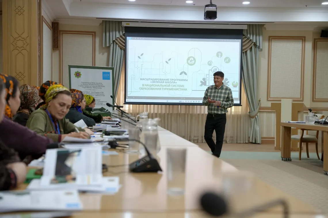 A presenter speaking to participants in front of a projection screen titled "Scaling up the Green School Programme in Turkmenistan's Education System".