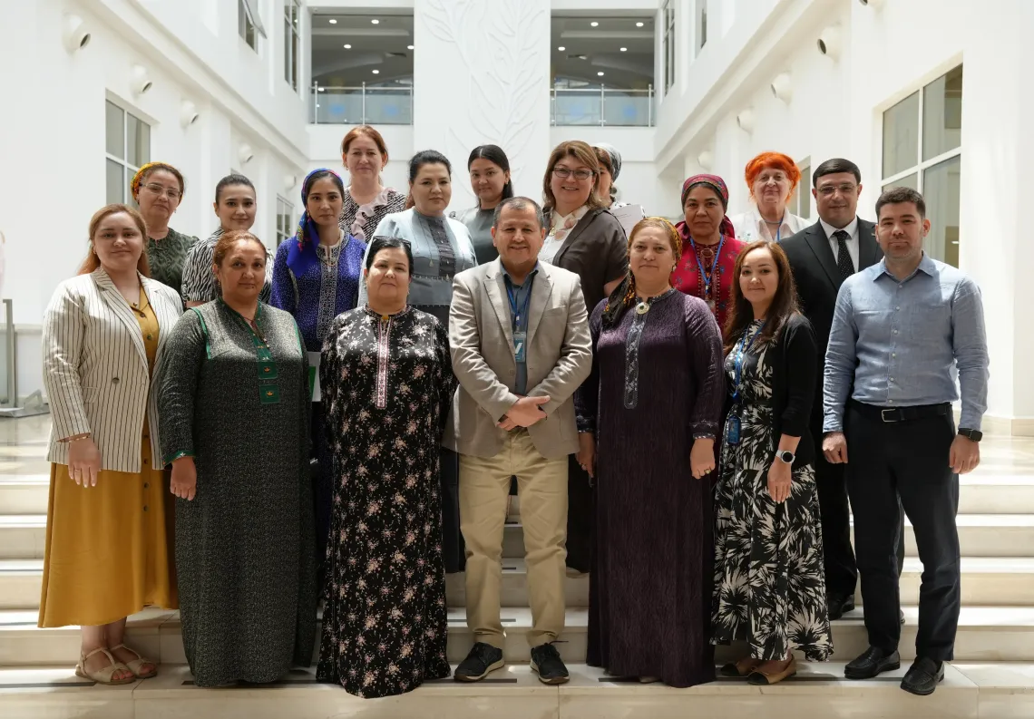 A group photo of workshop participants and organizers standing together on indoor steps inside a brightly lit, modern building atrium.