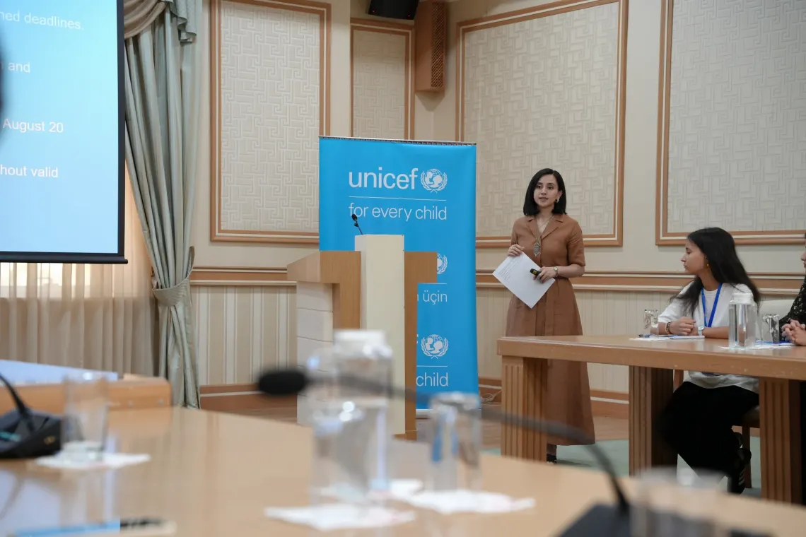 A woman spekaing in front of the audience behind her UNICEF banner