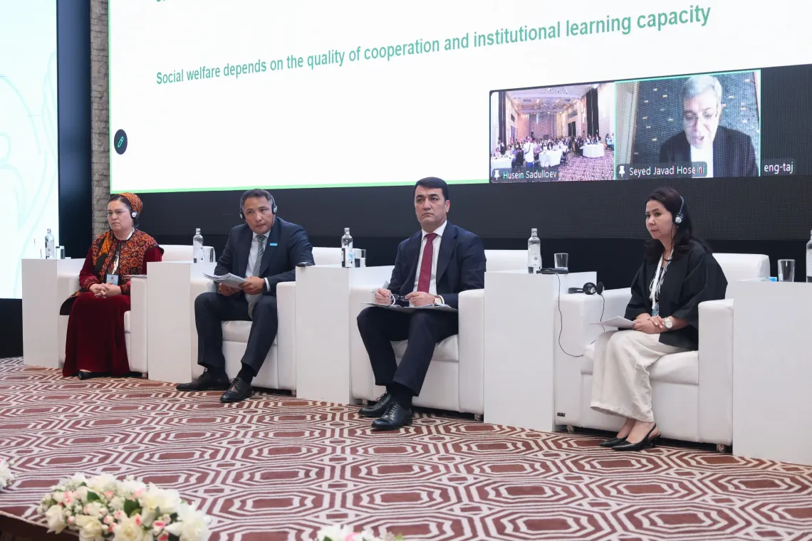 Four panel discussion participants seated in white armchairs on stage, wearing translation headsets during a presentation at the International Forum.