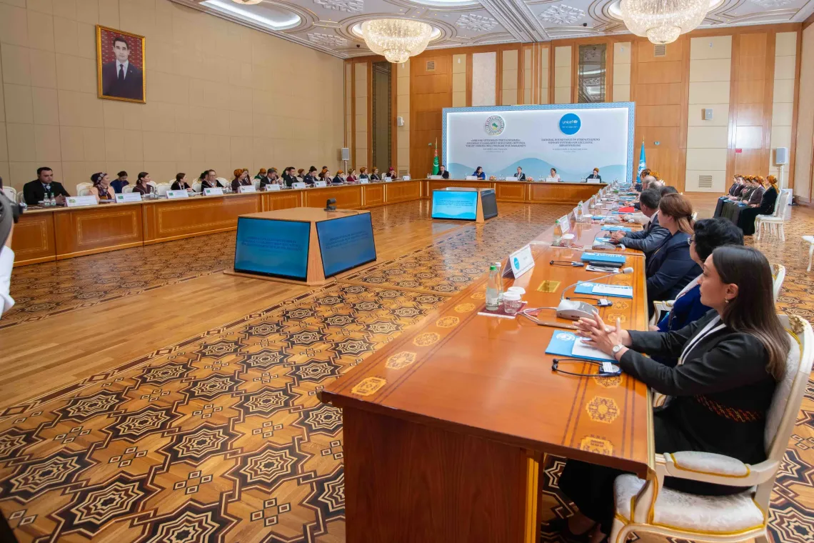 Wide shot of a large conference hall at Yyldyz Hotel with participants seated around a rectangular table setup for the National Roundtable on Exclusive Breastfeeding.