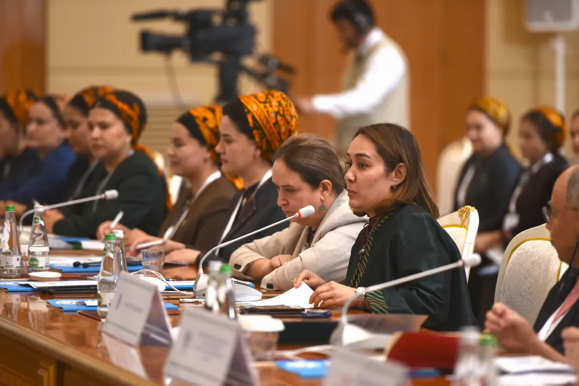 Side profile of conference participants seated at the table with microphones and official documents during a session.