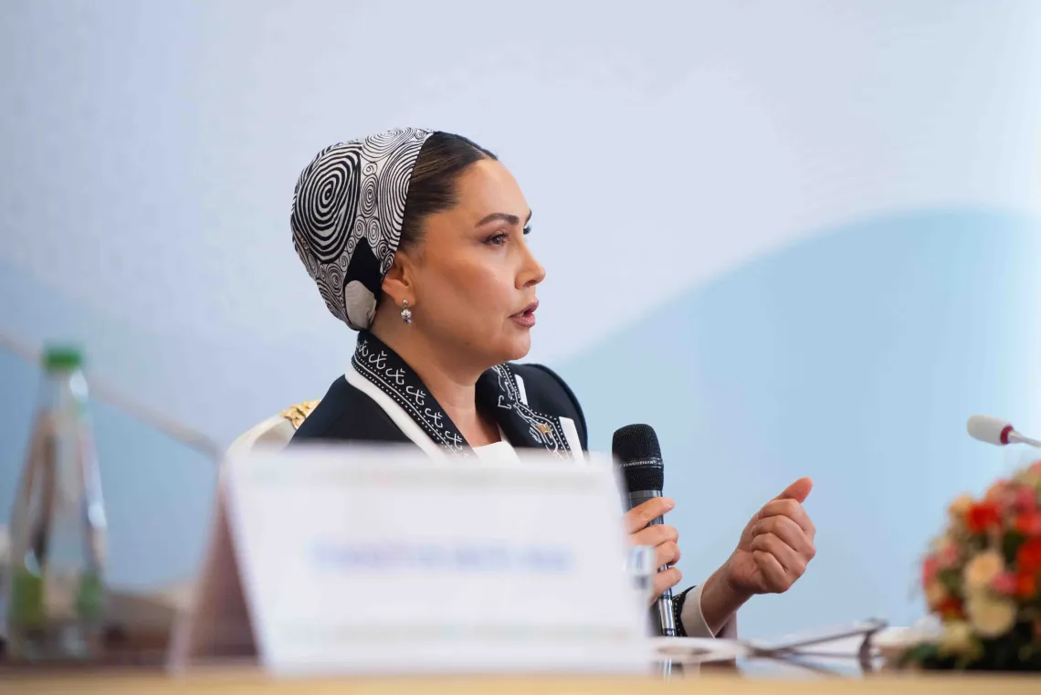 Medium close-up of Ms. Oguljahan Atabayeva speaking with hand gestures while holding a microphone.