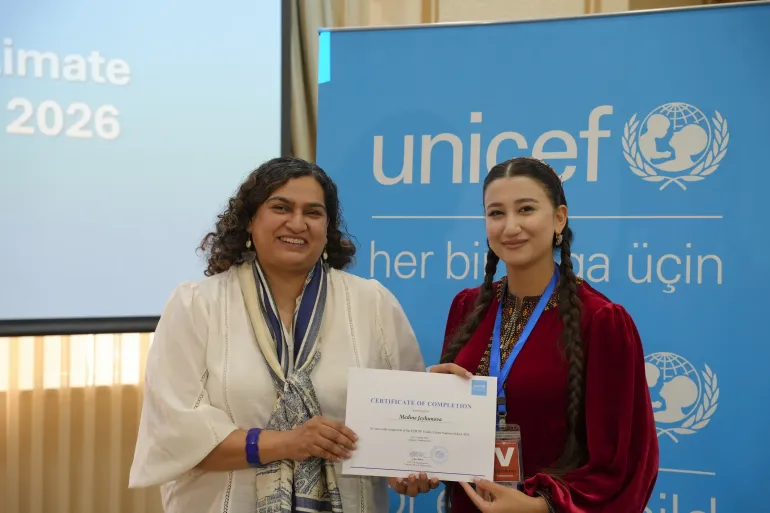 UNICEF Representative Jalpa Ratna presents a Certificate of Completion to a smiling young woman in front of a blue UNICEF banner.