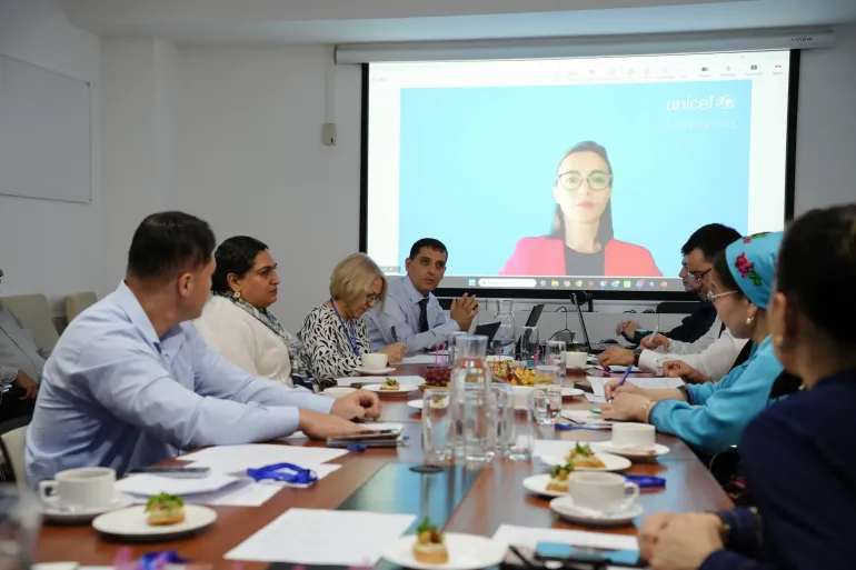 Participants seated around a meeting table watching an online presentation displayed on a large screen with the UNICEF logo.