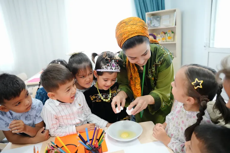 A preschool teacher guides children through a hands-on learning activity in a classroom.