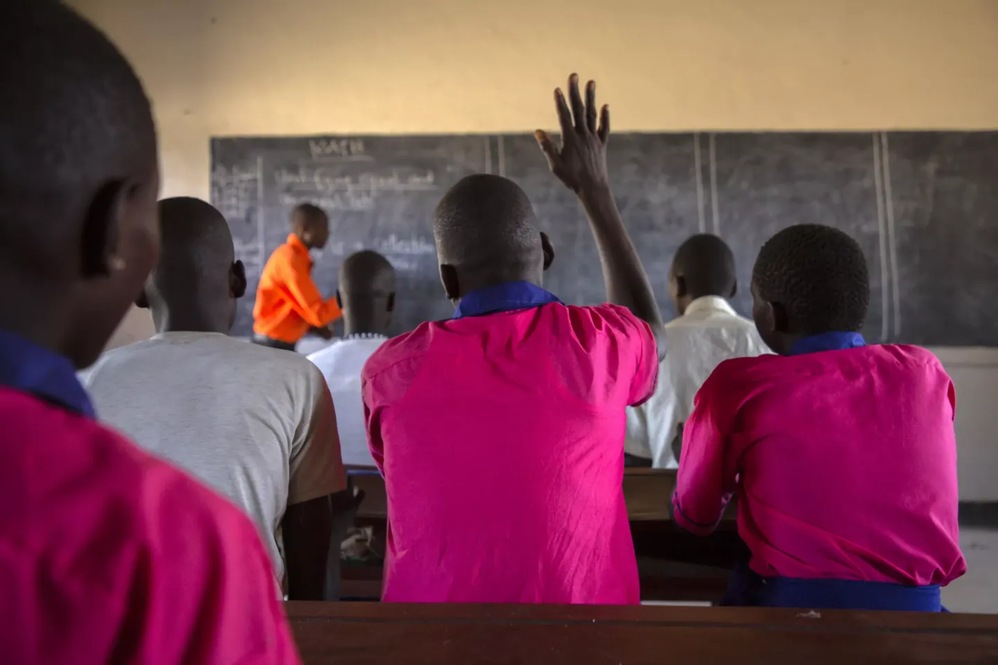 A primary six student at Lomuno Primary School Uganda, raises his hand to make a contribution during a mathematics class held by the teacher, Mr. Amos Chebrot (orange shirt).
